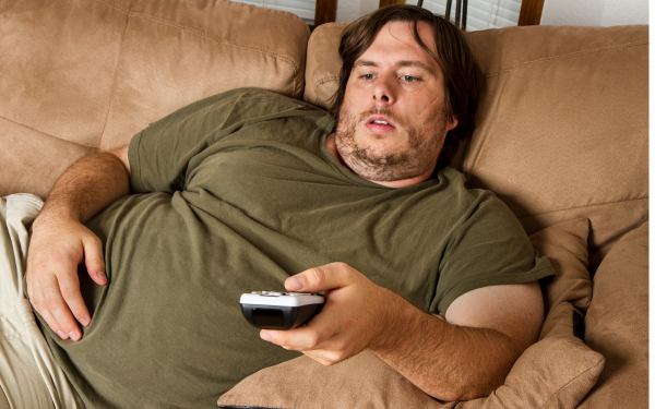 Middle-aged man slouching on couch with TV remote